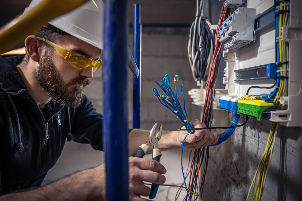 male-electrician-works-in-switchboard-with-an-electrical-connecting-cable(1)